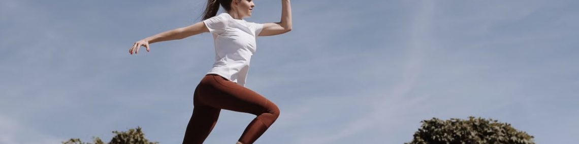 Athletic woman in action jump against a blue sky background. Captures fitness in motion.