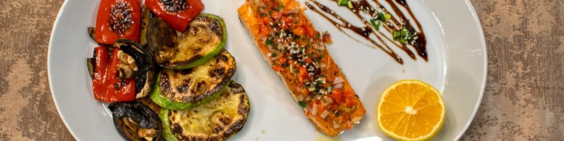 Gourmet grilled salmon served with roasted vegetables and lemon slice on a white plate.